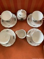 Top view of the set showing four coffee cups on their matching saucers, sugar pot with lid, and creamer on a red striped surface