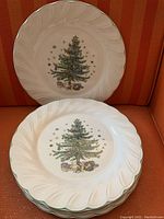 Four white ceramic dinner plates with scalloped edges, each decorated with a Christmas tree and presents in the center, photos taken to show the design and condition.
