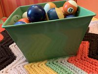 Green bin filled with billiard balls, including a visible ball numbered 13 and various striped and solid colors.