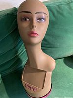 Front view of mannequin head showing facial features and base with brand Outre.