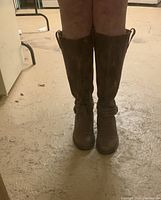 Front view of knee-high brown leather boots worn, showing rounded toe and smooth leather surface.