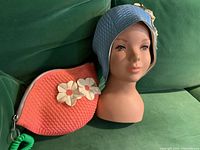 New retro baby blue swim cap with three white flowers on mannequin head beside coral pink quilted makeup bag with white flower appliques.