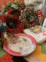 Overall view of vintage Christmas lot showing wreaths, Santa plates, napkins, elves, and tablecloth on colorful crochet blanket background