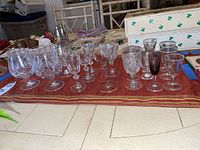 Wide angle photo showing various cut crystal wine glasses, etched glasses, snifters, and dessert glasses arranged in rows on a red patterned tablecloth.