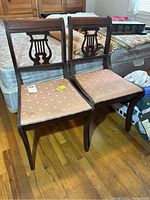 Front view of two matching antique wooden chairs with lyre backs, light peach upholstered seats with floral pattern, placed on wooden floor.