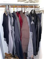 Photo of various coats, shirts, and shorts hung on hangers inside a closet showing overall lot contents.