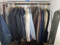 Closet rod with various men's suits, dress shirts, sweaters in assorted colors mostly blues, grays, whites, and neutrals, clothing hung on hangers.