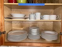 White ceramic Oneida Basketweave dinnerware stacked inside the cabinet: plates on bottom shelf, cups and bowls above.