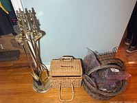 Photo showing brass fireplace tool set on round base, alongside two small woven wicker storage baskets and larger baskets in background.