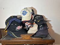 Front view of assorted baseball caps stacked on wooden surface showing various brand logos including Bud Racing and beige hockey cup champions cap.