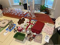 Photo of assorted holiday ornaments, ceramic dish, pewter salt and pepper shakers, napkin rings, red napkins, paper and linen napkins on a table with a red decorative runner and glassware in background