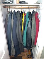 Full view of 11 assorted men's jackets hanging in closet showing variety of colors and materials including wool and leather.