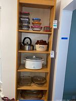 Full view of shelving with kitchenware items including storage containers, kettle, beanpot, crock pot and bakeware dishes placed