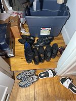 Overview of the assorted men's shoes gathered on a wooden floor next to a gray plastic bin