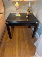 Two square black side tables with glossy marble-like enamel tops featuring white vein patterns, gold accents on corners and leg bottoms, placed on wooden floor next to walls.