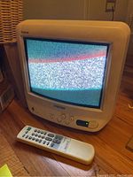Sony Trinitron TV displaying static with remote control placed in front on wooden floor.