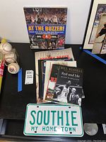 Multiple Boston sports books including 'At The Buzzer!', 'Historic Boston Hockey', and Bill Russell's 'Red and Me' alongside a Southie vanity plate.