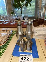 Two sets of sterling silver salt and pepper shakers on blue cloth with glasses and napkins in background.