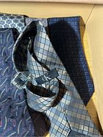 Close-up of Calvin Klein metallic silver checkered necktie with CK logo tag, plus dark checkered and paisley ties.