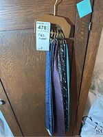 Six mens neckties of different colors and patterns on a wooden hanger hung on a door.