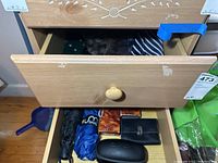 View of two drawers showing ties, umbrellas, cologne, and cases inside wooden dresser drawers.