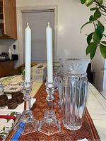 Two clear crystal Tiffany & Co candle holders with slender tops and octagonal bases beside a tall faceted clear crystal vase with cut starburst patterns on the rim.