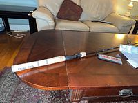 Photo showing full view of the Ugly Stik Elite 88 fishing rod placed on wooden table with white grip handle and black rod body.