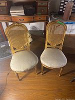 Front view of both chairs showing gold frames, cane backs and cream upholstered seats