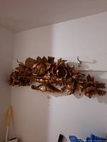 Full view of the carved floral wall plaque mounted on a white wall, showing the entire horizontal piece with hooks above it.