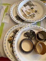First photo shows multiple bangles on one plate, and various earrings, rings, and brooches on another plate, all costume jewelry.