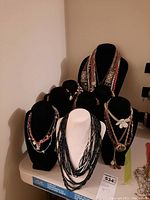 Six necklaces displayed on six velvet necklace stands in black and white.