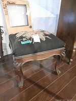 Full view of square wood footstool with black needlepoint floral upholstery and carved wooden legs.