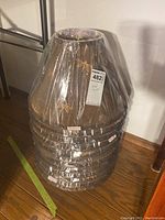 Stack of twelve brown fabric lampshades wrapped in protective plastic, showing general shape and packaging.
