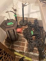 Lantern, bird feeder stand, and cast metal wall decor pieces arranged on brick floor with price tags visible.