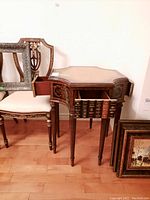 Front‐angle shot showing table with two side drawers open and decorative framed chair to left.