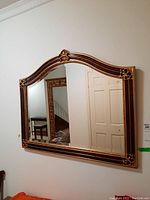 Full view of the framed wall mirror hung on the wall showing the shape and decorative details.