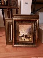 Three framed paintings positioned leaning against a wall, showing the fronts and frames.