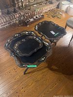 Two wood stands with three removable black trays decorated with gold floral accents arranged on a wooden floor near a fireplace.