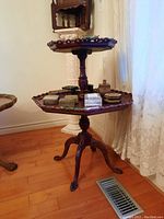 Full view of two-tier wooden table with decorative scalloped edges on tiers, holding various small boxes not included in sale.