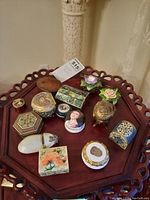 Top view of eleven diverse trinket boxes displayed on a wooden table, showing varied shapes, colors, and decorative motifs.