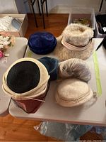 Top view of the six vintage hats placed on a table showing different styles and textures, including fur, velvet, and woven materials.