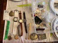 Overview photo of five wristwatches, a pocket watch, assorted cufflinks, belt buckles, and watch straps displayed on a table
