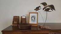 Overview of lot showing carved wood bookends, round wooden bowl, copper bird sculpture on stone base, and framed art print.