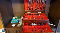 Wooden canteen open revealing red velvet lined trays with assorted stainless steel cutlery