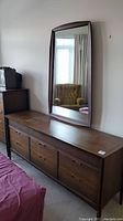 Front and side view of the nine-drawer dresser topped with a large attached curved mirror showing its dark wood finish and mid-century modern design.