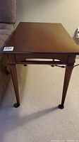 Side view of one wooden end table showing tapered legs and casters