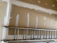 Full length side view of aluminum extension ladder against a drywall garage wall