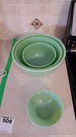 Three jadeite swirl mixing bowls nested with one plain bowl in front on countertop.