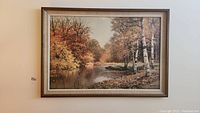 Overall view of the framed print showing an autumn river landscape with fall foliage and a neutral toned frame.