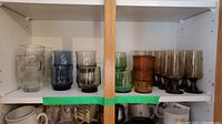 Eight mixed MCM-style drinking glasses with gold leaf accents, frosted, blue and amber tinted glasses on shelf
